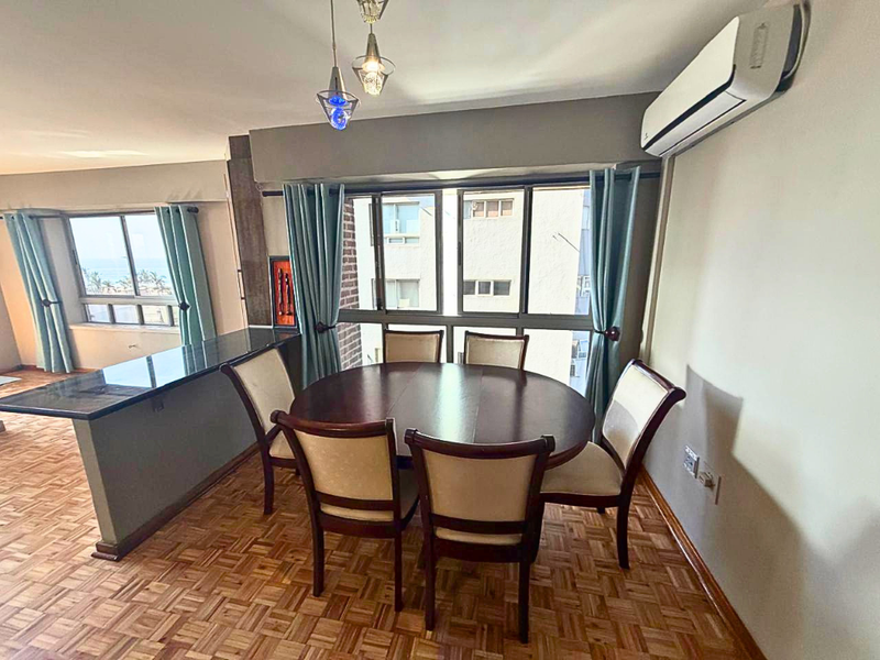 Open-plan dining area featuring parquet flooring, a breakfast bar, and a wall-mounted split-system air conditioner with views through large aluminium-framed windows.
