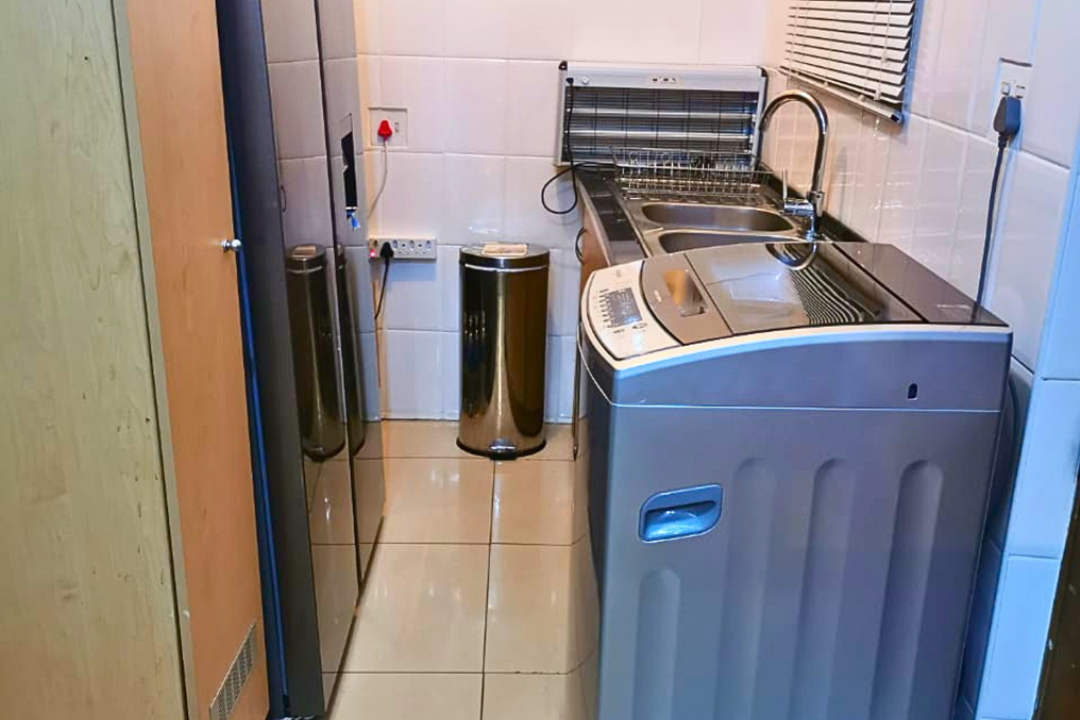 Compact laundry area featuring tiled walls and flooring, a stainless steel sink with mixer tap, and space for laundry appliances.