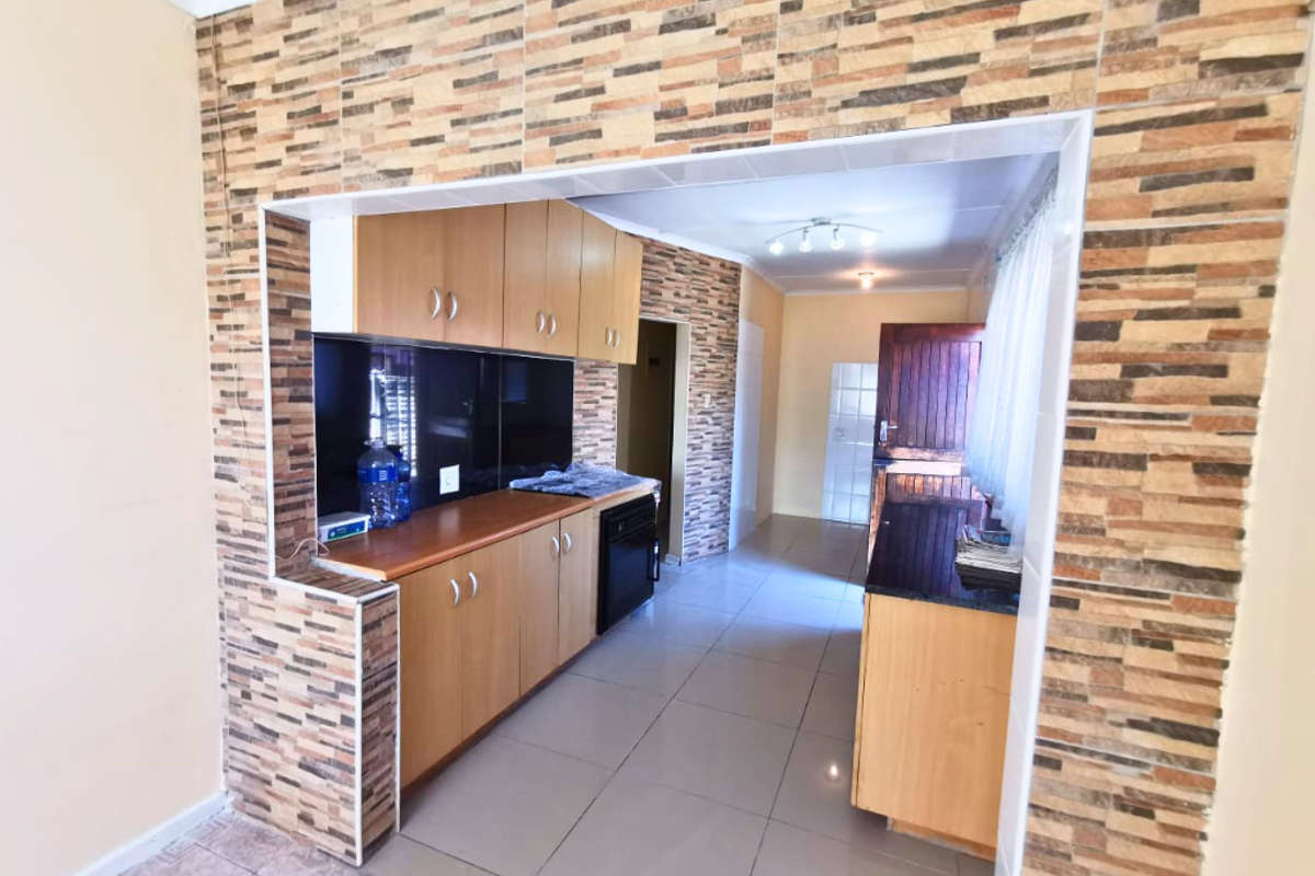 A functional kitchen featuring laminate cabinetry, stone-look wall cladding, and ceramic floor tiles, offering a practical layout with built-in cooking appliances.