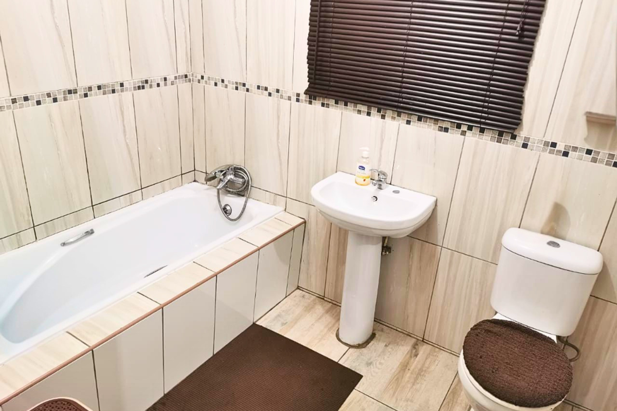 A functional bathroom featuring a built-in bathtub, pedestal basin, and toilet, finished with neutral wall and floor tiling.