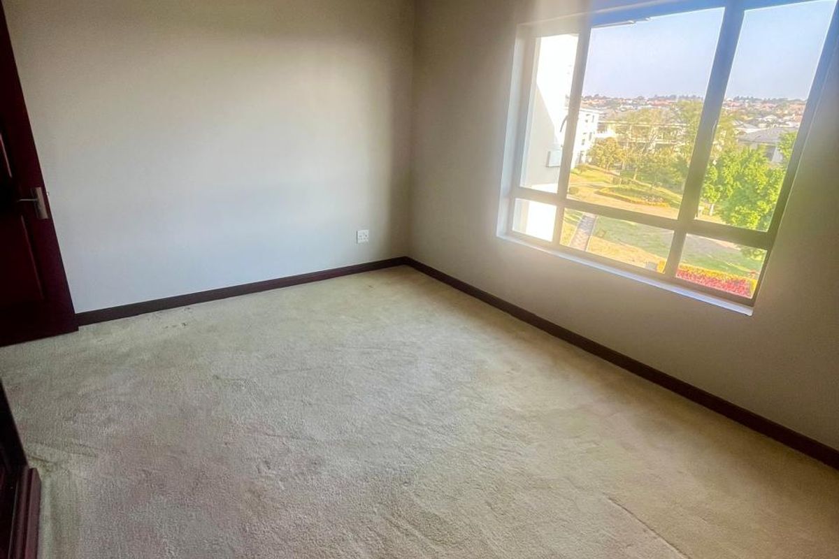 A vacant bedroom featuring neutral carpet flooring, dark timber skirting boards, and a large window providing natural light and neighborhood views.