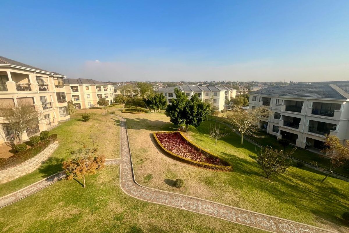 An elevated aerial view of the apartment complex grounds, featuring well-maintained lawns, landscaped garden beds, and paved walkways between residential buildings.