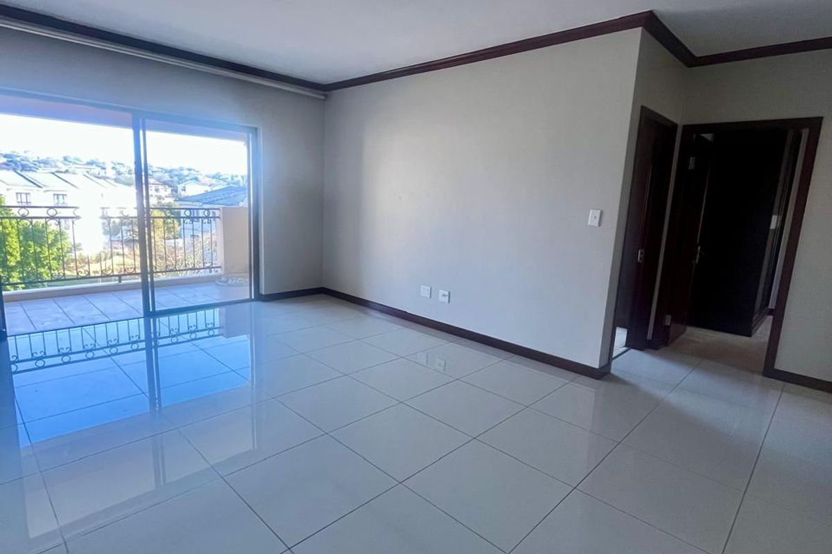 A bright, empty living room featuring polished tiled floors, dark wood-tone trim, and a sliding glass door leading to an outdoor balcony.