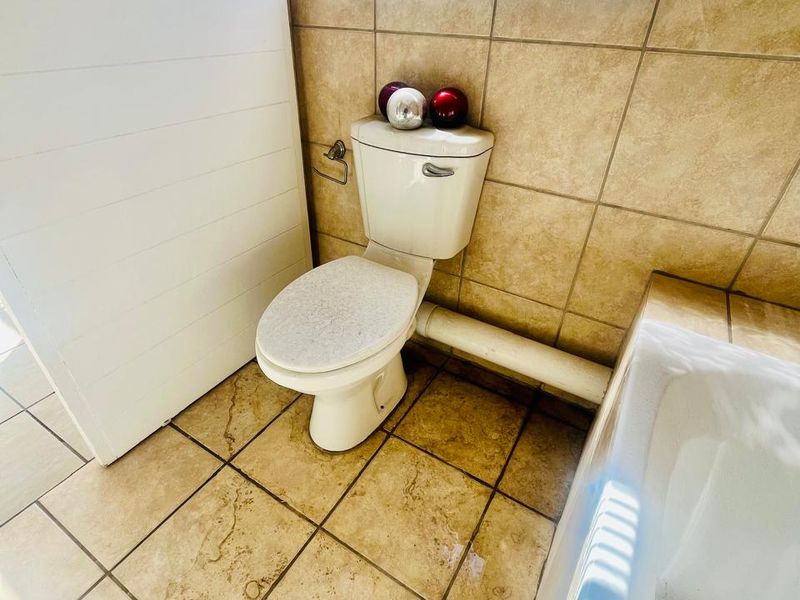 A functional bathroom featuring ceramic tiling, a standard toilet, and a bathtub, with an exposed plumbing pipe along the wall.