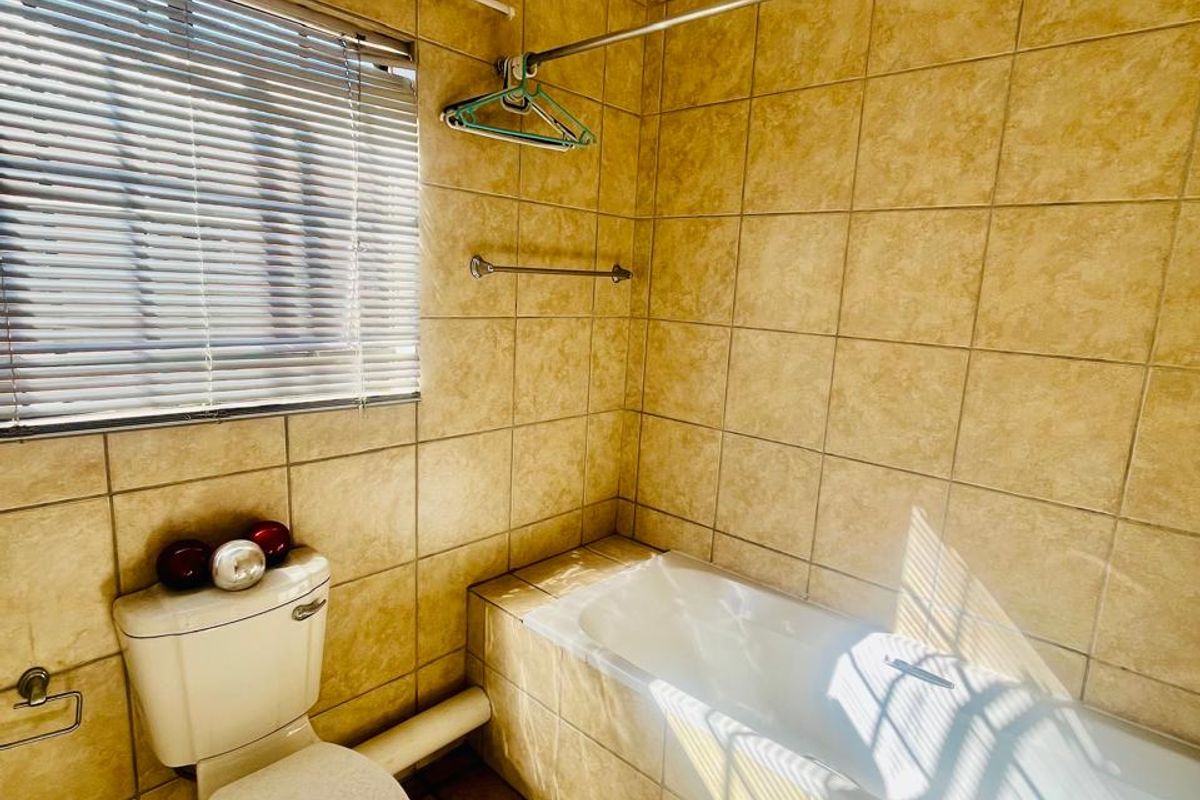A dated bathroom featuring full-height wall tiling, a standard bathtub, and a toilet, with visible exposed plumbing and an aging extractor fan.