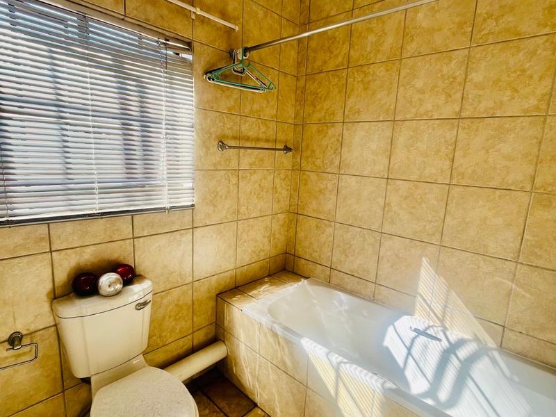 A dated bathroom featuring full-height wall tiling, a standard bathtub, and a toilet, with visible exposed plumbing and an aging extractor fan.