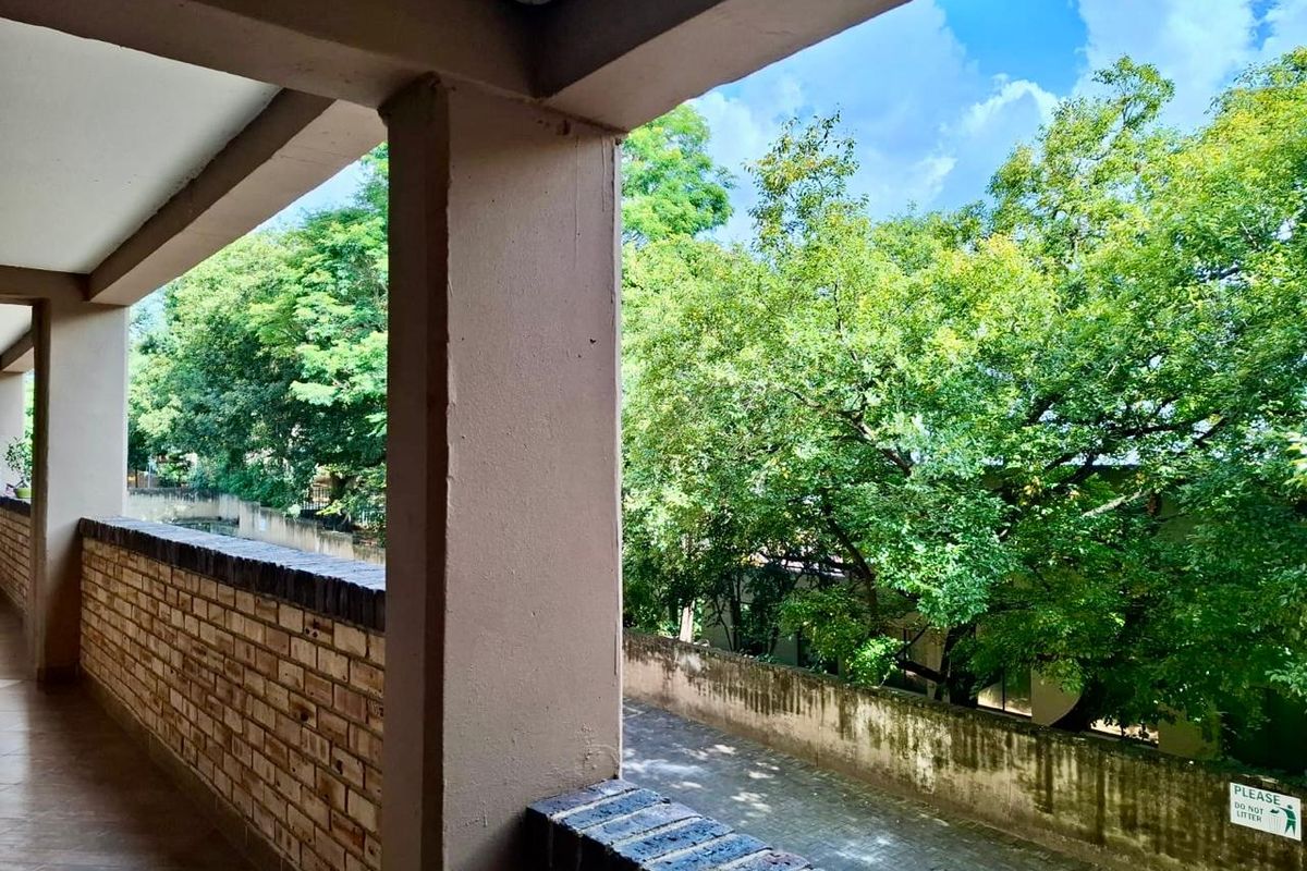 A covered balcony featuring a brick balustrade and tiled flooring, overlooking a leafy outdoor area.