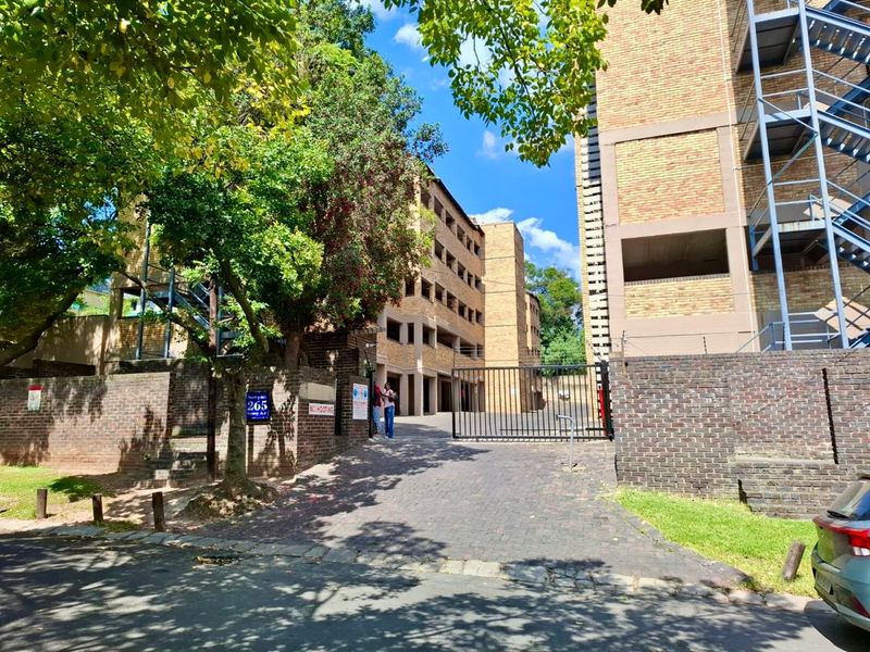 Front exterior view of a multi-story brick apartment complex featuring a paved driveway, secure metal gate, and external staircase access.