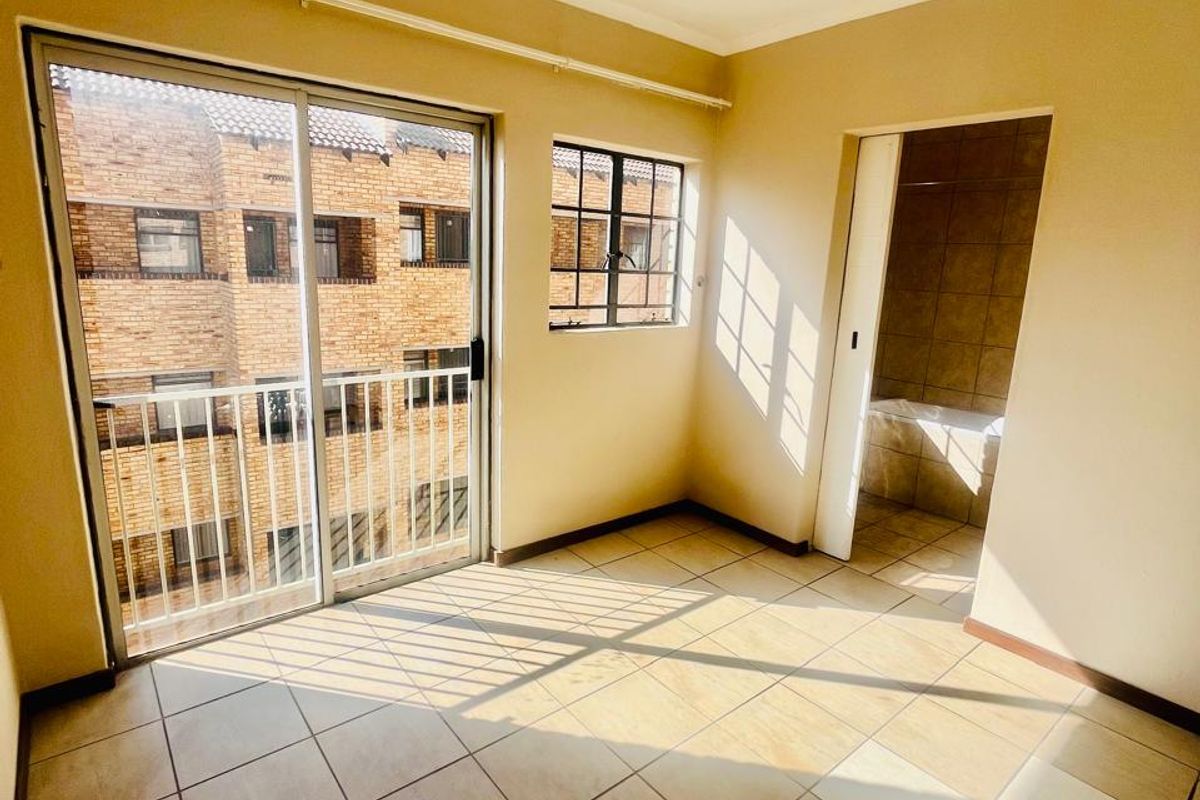 An empty bedroom featuring tiled flooring, a sliding glass door leading to a balcony, and an en-suite bathroom entrance.