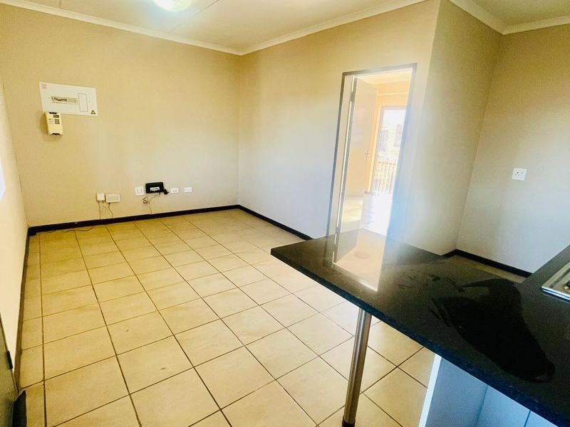 An empty open-plan living and kitchen area featuring tiled flooring and a granite breakfast bar, providing a versatile space for living and dining.