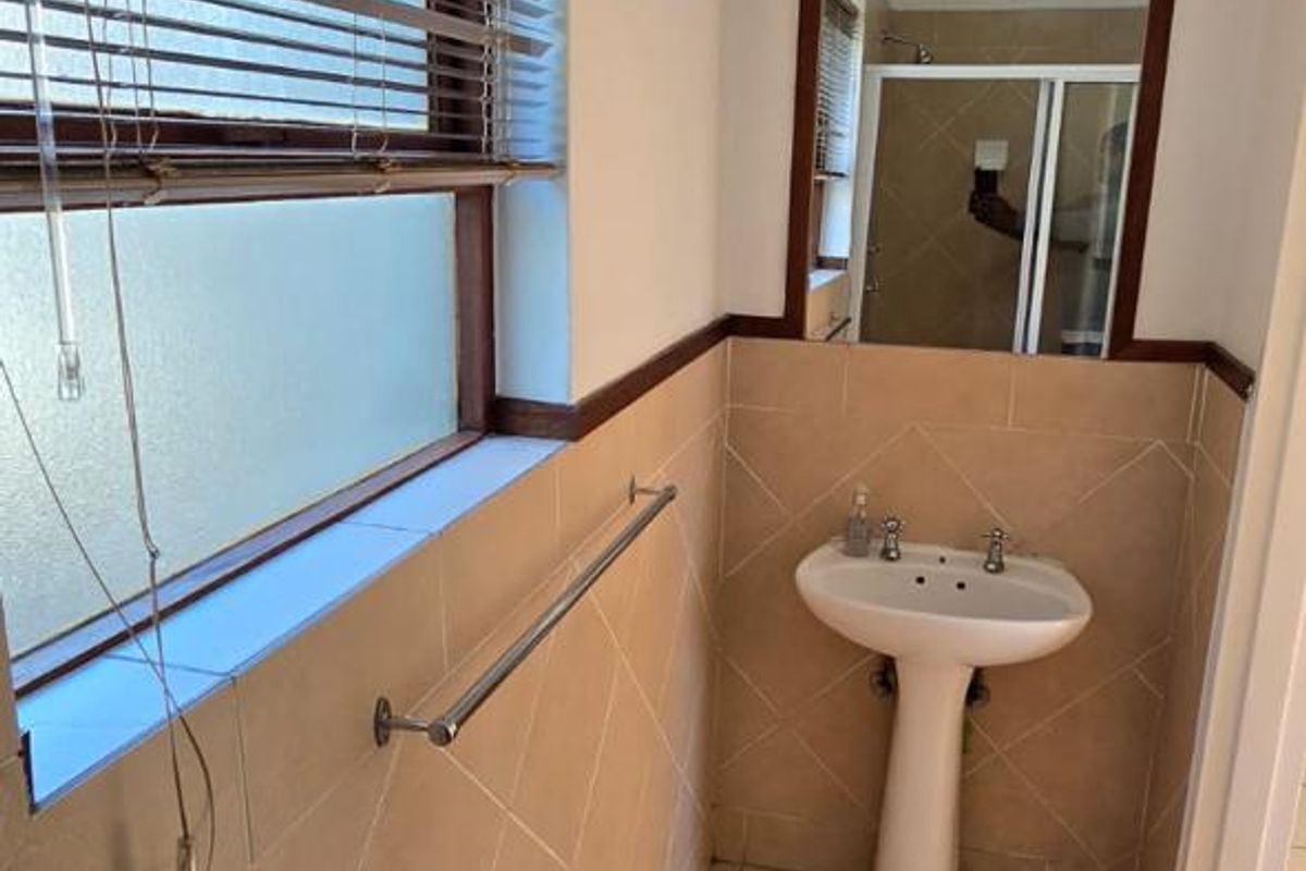 A functional bathroom featuring a pedestal basin, tiled walls and flooring, and a wall-mounted mirror, offering a clean and practical space.