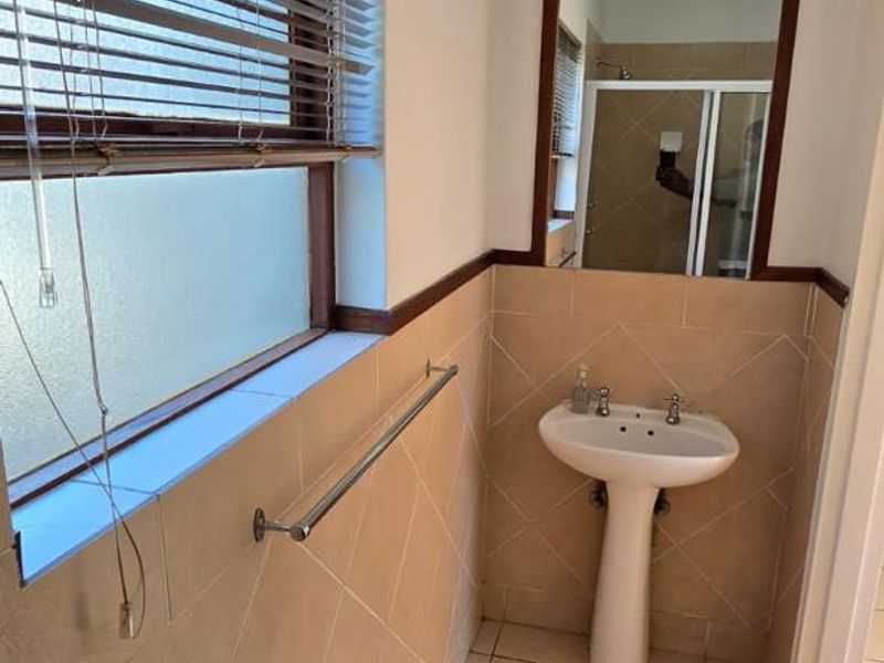 A functional bathroom featuring a pedestal basin, tiled walls and flooring, and a wall-mounted mirror, offering a clean and practical space.