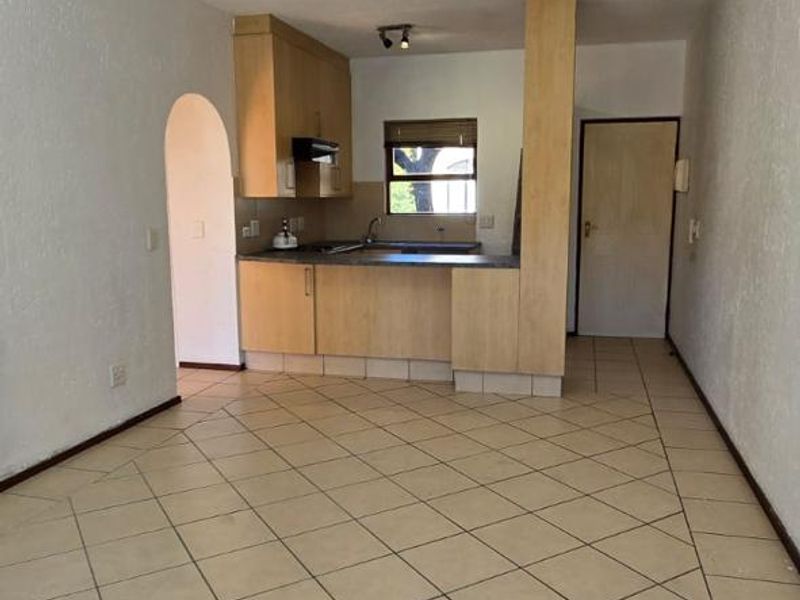 An open-plan living and kitchen area featuring tiled flooring, built-in wooden cabinetry, and a functional kitchen layout with an archway entrance.