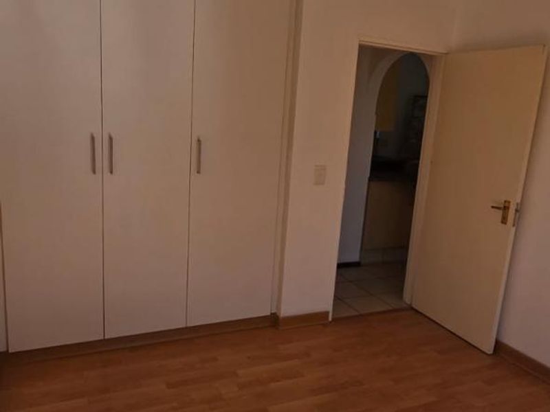 A bright, empty bedroom featuring laminate flooring, built-in cupboards, and a ceiling fan, offering a clean canvas for personalization.
