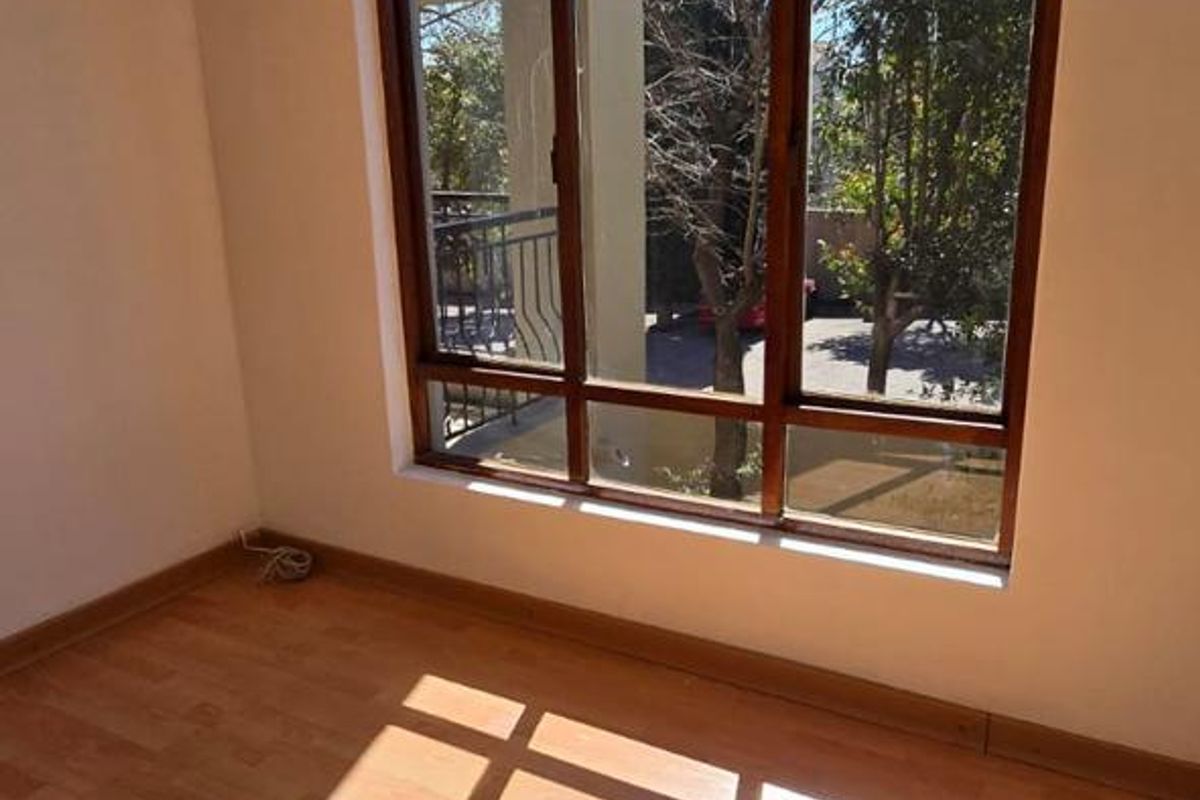 A bright, empty bedroom featuring laminate flooring and a large arched window that allows for ample natural light.