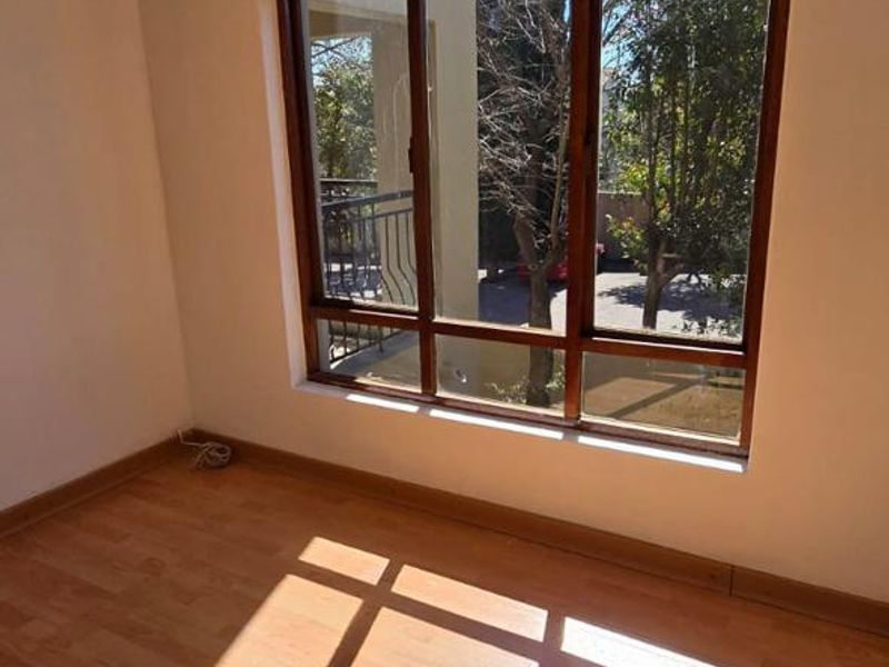 A bright, empty bedroom featuring laminate flooring and a large arched window that allows for ample natural light.