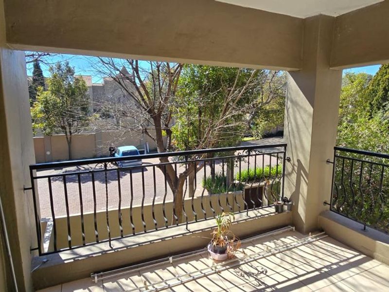 A covered balcony featuring tiled flooring and a wrought iron balustrade, offering an outdoor space with views of the surrounding area.