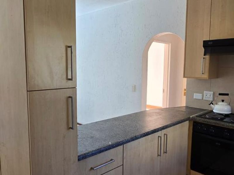 A functional kitchen featuring light wood-tone cabinetry, dark laminate countertops, built-in oven, extractor fan, and ceramic floor tiles with an adjacent arched doorway.