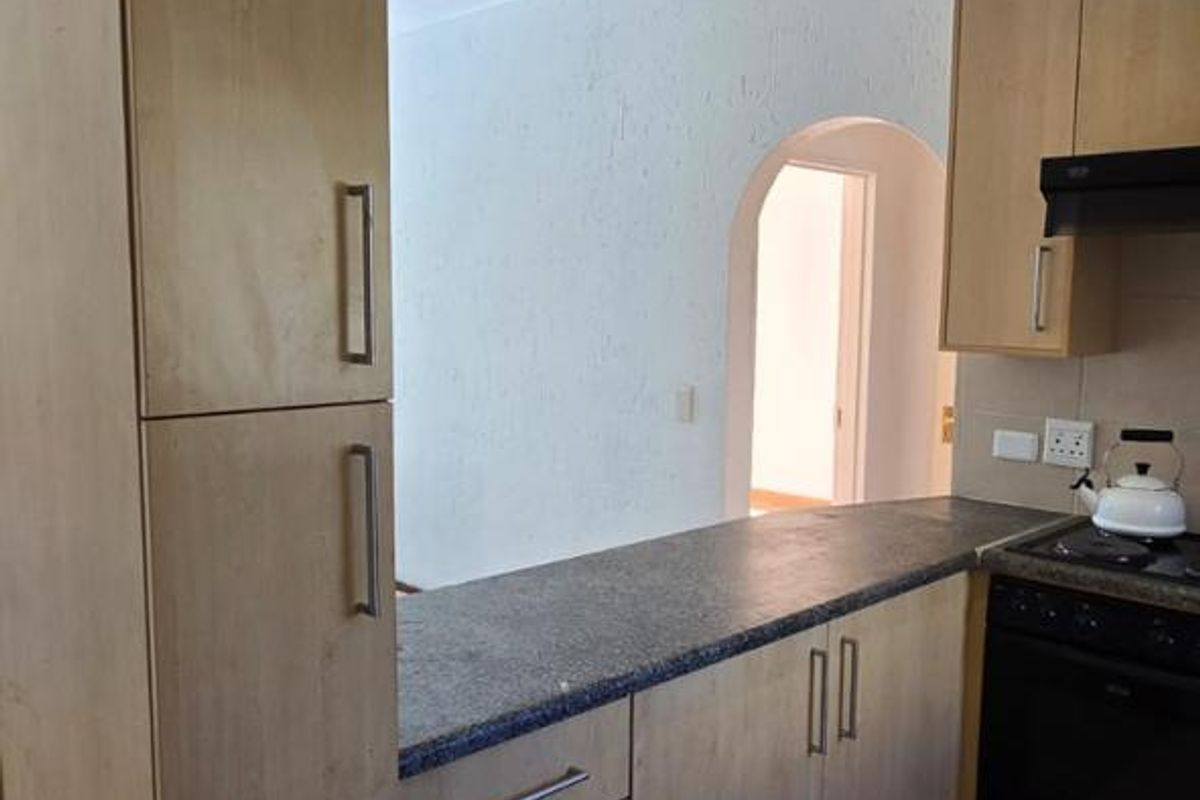 A functional kitchen featuring light wood-tone cabinetry, dark laminate countertops, built-in oven, extractor fan, and ceramic floor tiles with an adjacent arched doorway.