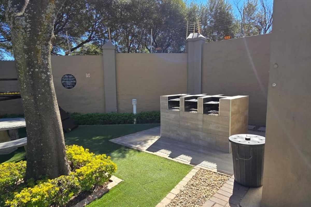Communal outdoor area featuring a built-in braai station, artificial lawn, and secure perimeter walling.
