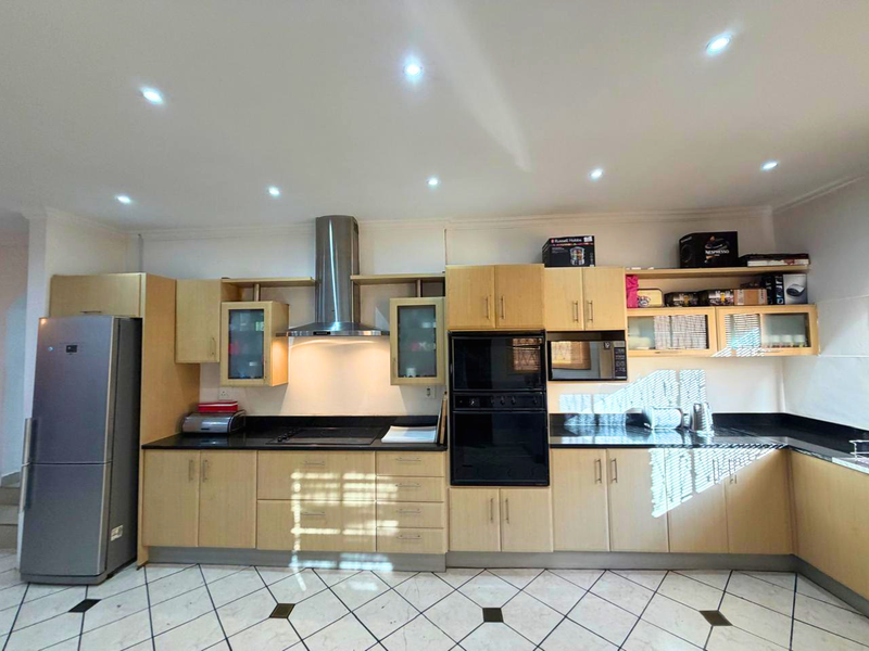 A functional kitchen featuring light wood cabinetry, granite countertops, built-in oven and microwave, stainless steel extractor fan, and tiled flooring with decorative inserts.