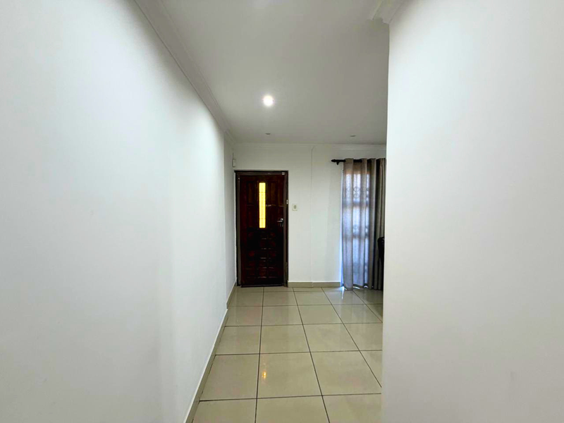 A clean, neutral hallway featuring tiled flooring, recessed lighting, and a solid timber entrance door, providing a bright and welcoming transition space.