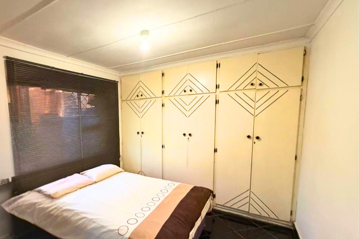 A bedroom featuring built-in cupboards with geometric detailing, dark tiled flooring, and venetian blinds.
