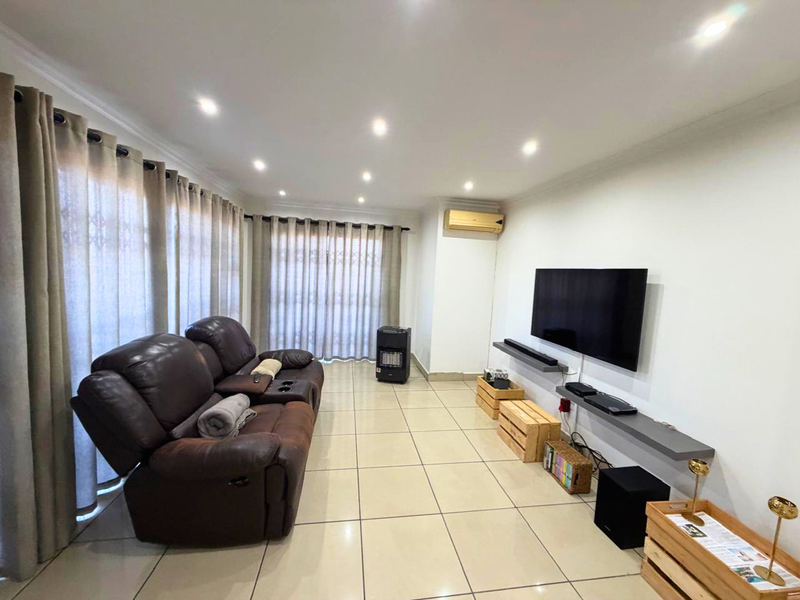 A bright living room featuring tiled flooring, recessed downlighting, a wall-mounted air conditioning unit, and a floating media shelf.