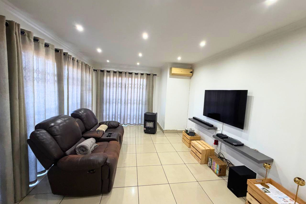 A bright living room featuring tiled flooring, recessed downlighting, a wall-mounted air conditioning unit, and a floating media shelf.