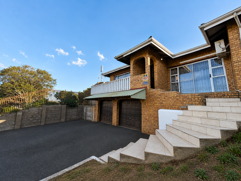 Front elevation of a brick house featuring a double garage, tiled staircase leading to an elevated entrance, and a balcony with a balustrade.