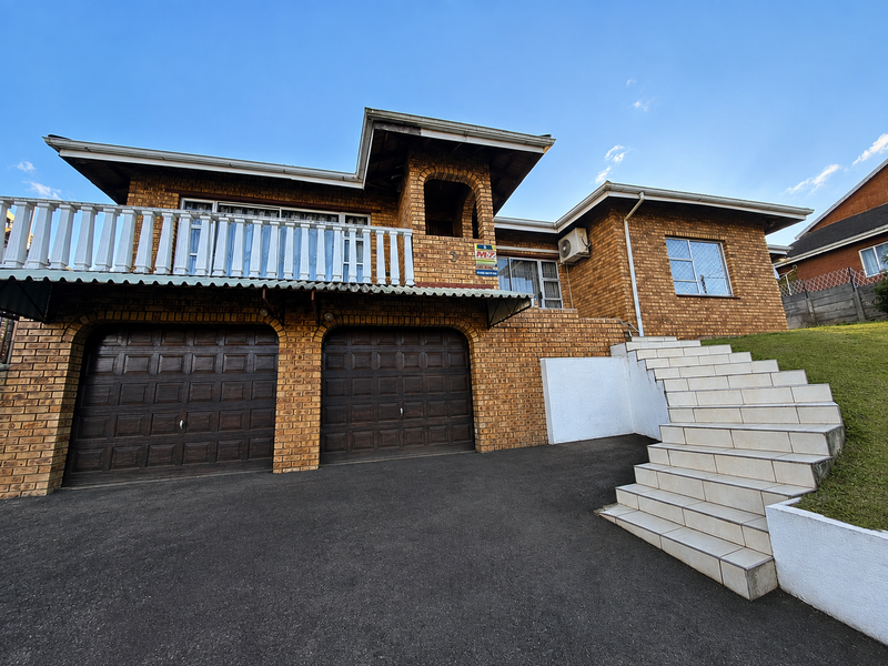 Front elevation of a double-story brick house featuring a double garage, an upper-level balcony, and a tiled staircase leading to the entrance.