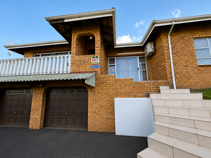 Front elevation of a face brick house featuring a double garage, elevated balcony with balustrade, and tiled entrance staircase.