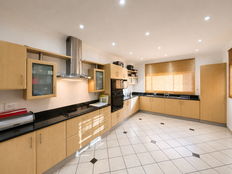 Spacious kitchen featuring light wood cabinetry, black granite countertops, integrated stainless steel appliances, and tiled flooring with decorative accents.