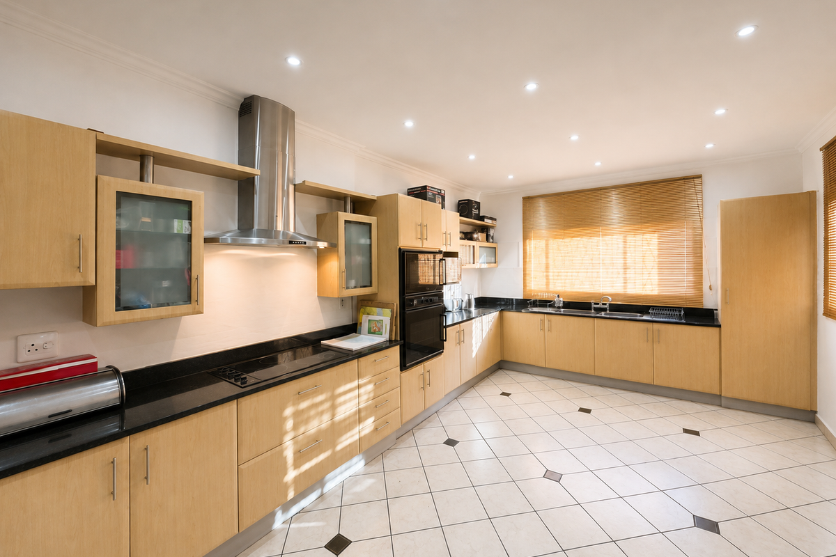 Spacious kitchen featuring light wood cabinetry, black granite countertops, integrated stainless steel appliances, and tiled flooring with decorative accents.