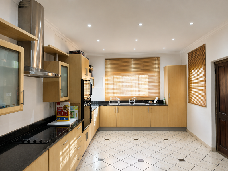 A well-maintained kitchen featuring light wood cabinetry, granite countertops, a built-in oven, electric hob, and stainless steel extractor fan with tiled flooring.