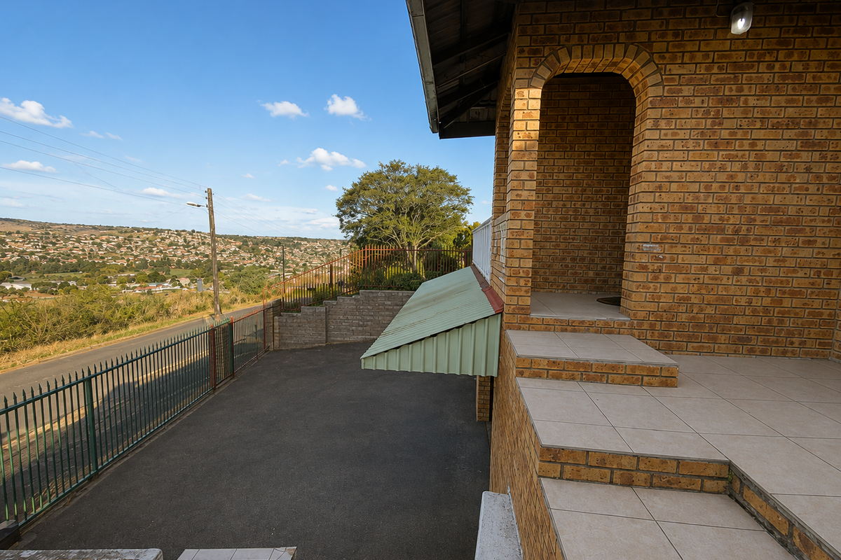 Rear exterior view featuring a tiled patio, face brick facade, metal awning, and a paved driveway overlooking the surrounding landscape.