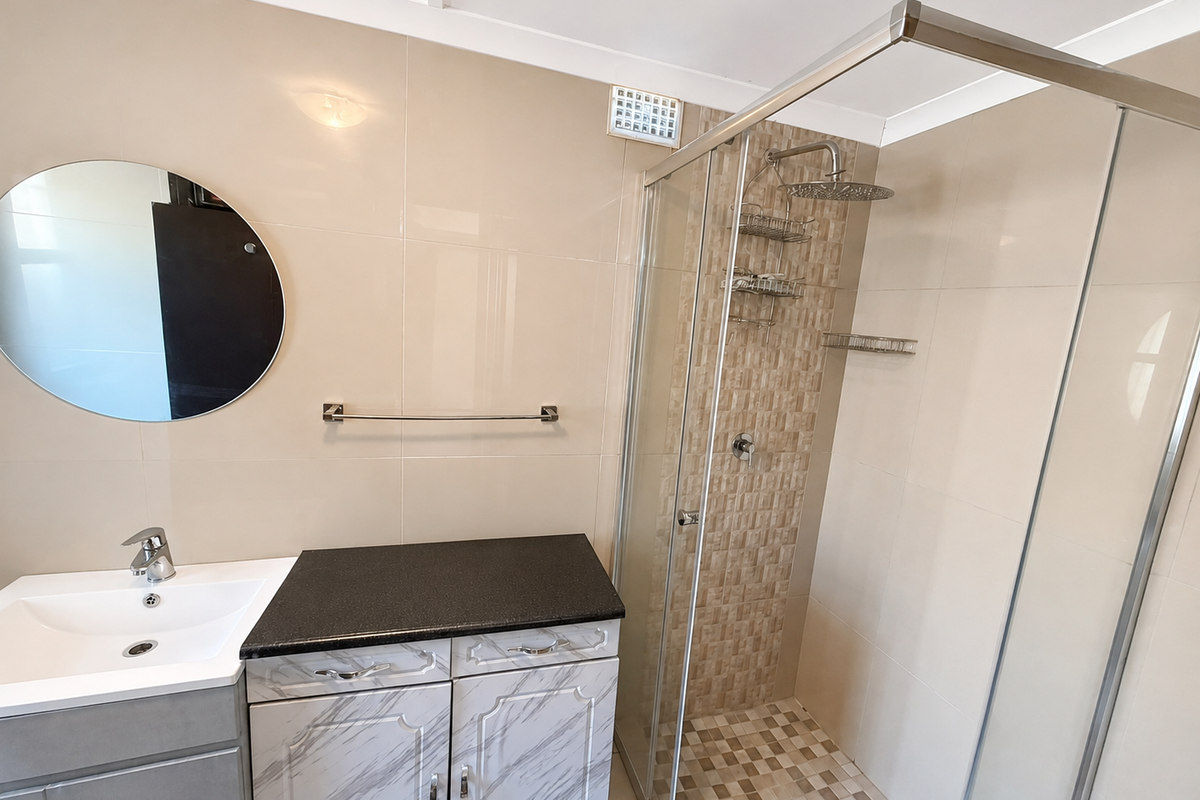 Modern bathroom featuring a vanity with stone countertop, basin, and a glass-enclosed shower with tiled feature wall and floor.