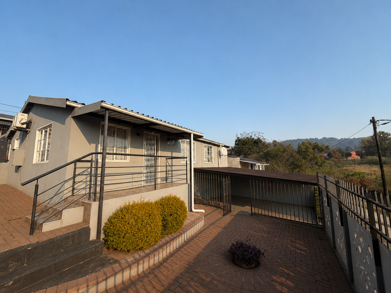Front exterior view of the house featuring a paved driveway, metal security railings, and a covered carport area.