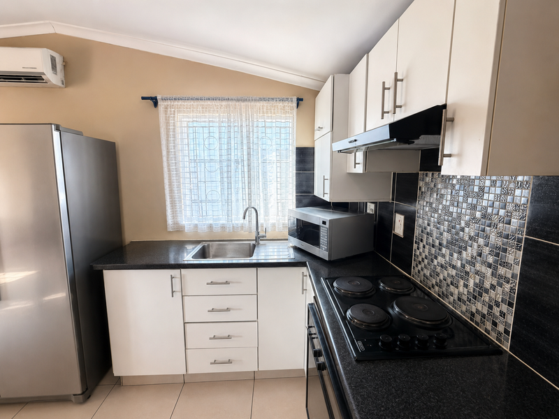 Compact kitchen featuring white cabinetry, dark granite countertops, a mosaic tiled backsplash, and integrated appliances including an electric hob and extractor fan.