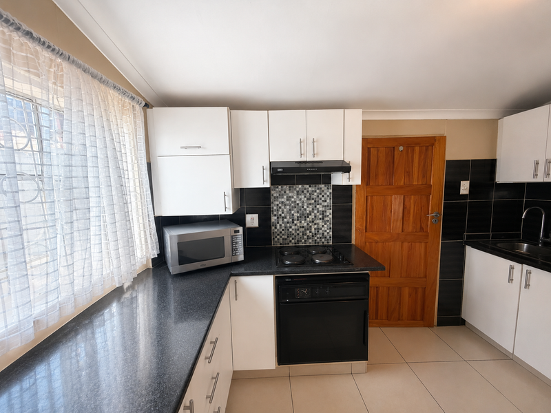 A functional kitchen featuring white cabinetry, dark laminate countertops, a mosaic tile backsplash, and integrated cooking appliances with tiled flooring.