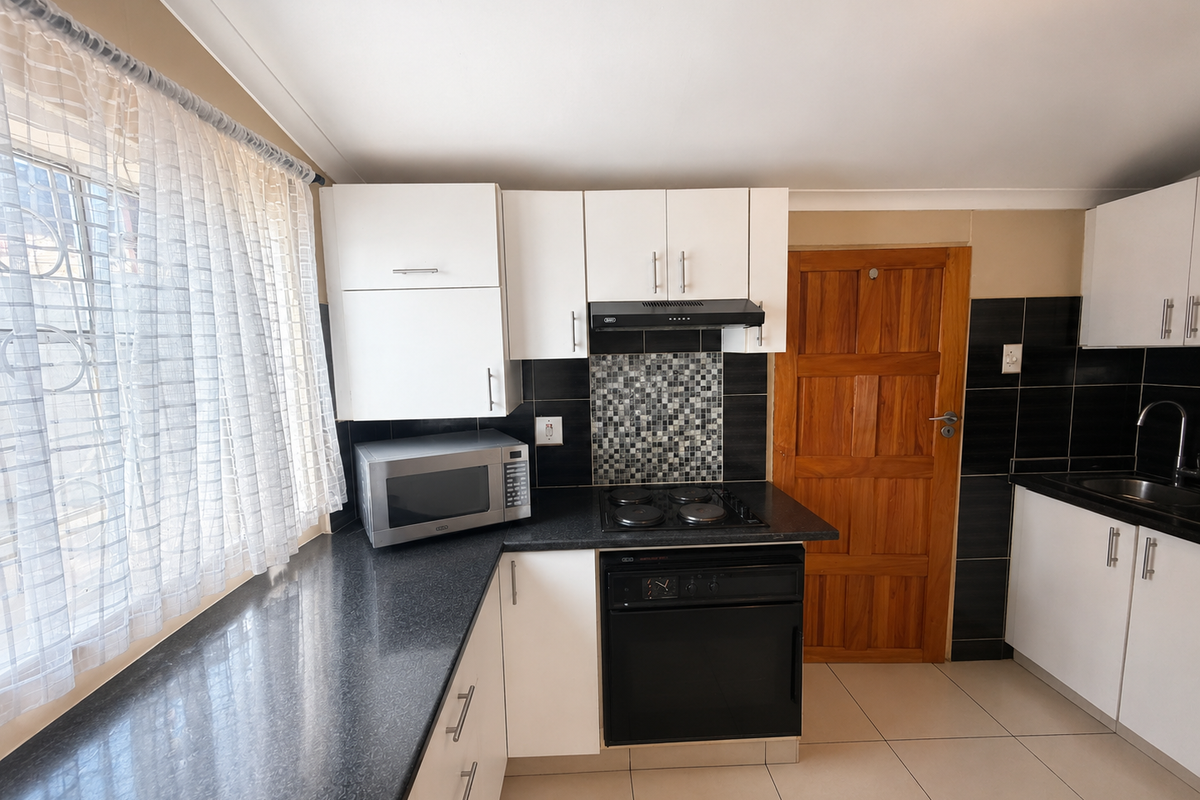 A functional kitchen featuring white cabinetry, dark laminate countertops, a mosaic tile backsplash, and integrated cooking appliances with tiled flooring.