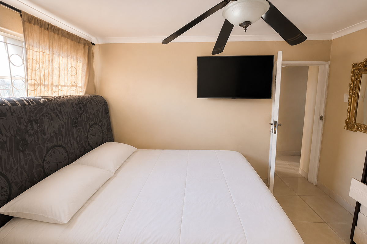 A bedroom featuring tiled flooring, a ceiling fan, and a wall-mounted television, with access to an adjoining room.