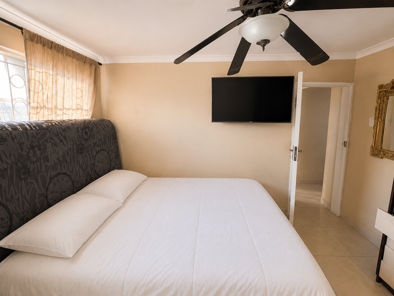 A bedroom featuring tiled flooring, a ceiling fan, and a wall-mounted television, with access to an adjoining room.