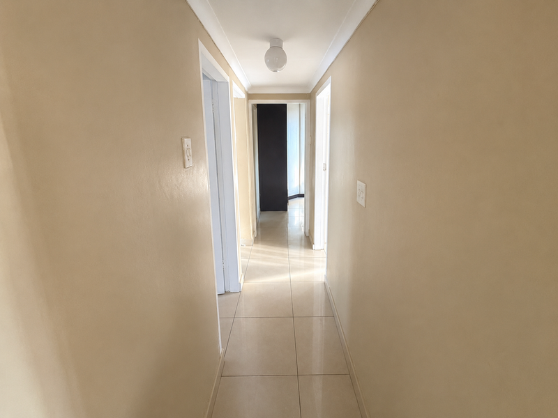 A clean, neutral-toned hallway featuring tiled flooring and simple ceiling lighting, providing access to multiple rooms within the home.