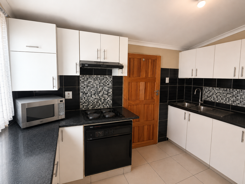 A well-maintained kitchen featuring white cabinetry, black granite countertops, mosaic tile backsplash, built-in oven, hob, and a stainless steel double sink.