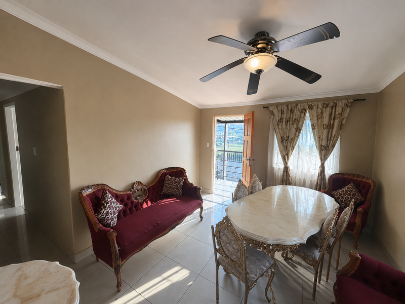 A well-maintained dining room featuring tiled flooring, coved cornicing, and a ceiling fan, with direct access to an outdoor balcony area.