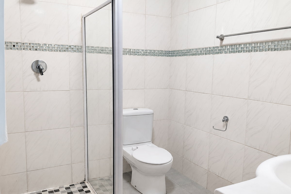 A clean, functional bathroom featuring a glass-enclosed shower, white toilet, and neutral wall tiling with a decorative mosaic accent border.
