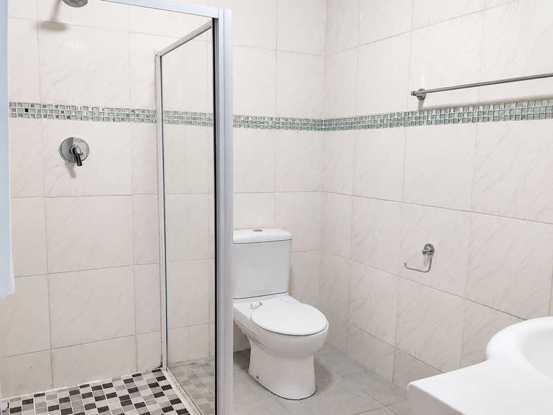 A clean, functional bathroom featuring a glass-enclosed shower, white toilet, and neutral wall tiling with a decorative mosaic accent border.