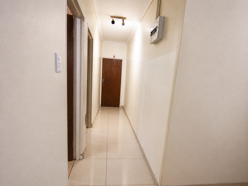 A clean, well-lit hallway featuring neutral tiled flooring and a wall-mounted electrical distribution board.