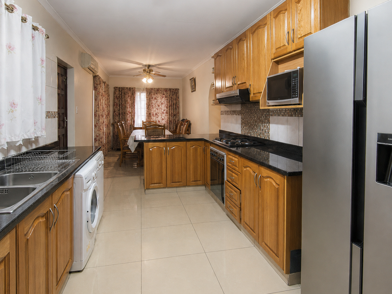 Open-plan kitchen and dining area featuring wooden cabinetry, granite countertops, built-in appliances, and tiled flooring, leading to a connected dining space.